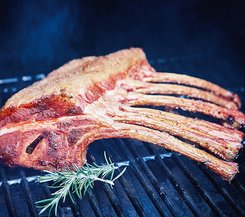 Gegrilltes Schweinetomahawk mit Rosmarin Ein gegrilltes Schweinetomahawk mit Rosmarinzweig auf einem Grillrost, umgeben von Rauch.