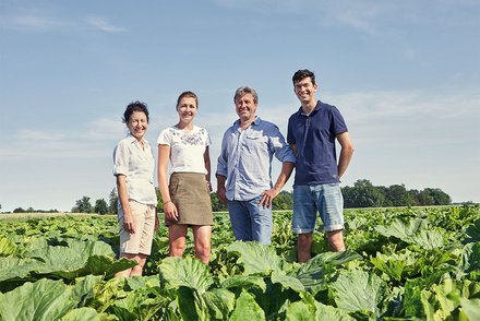 Team auf dem Gemüsefeld Eine Gruppe von vier Personen, zwei Männer und zwei Frauen, steht lächelnd in einem großen Gemüsefeld bei sonnigem Wetter.
