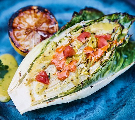 Gegrilltes Salatherz mit Tomaten und Dressing Gegrilltes Salatherz mit Tomaten und Dressing auf einem blauen Teller