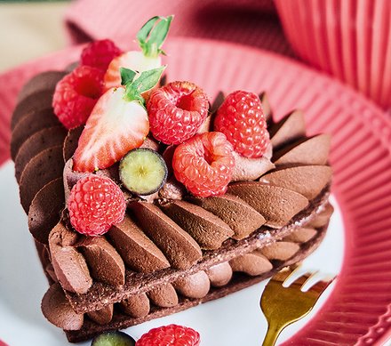 Schokoladentorte mit frischen Beeren Ein Stück Schokoladentorte, dekoriert mit frischen Himbeeren, Erdbeeren und Trauben, auf einem rosa Teller.