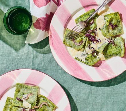 Bärlauch-Ravioli Zwei Teller mit Bärlauch-Ravioli, garniert mit roten Zwiebeln und serviert in einer cremigen Sauce, auf einem grünen Tisch mit rosa-weiß gestreiften Tellern