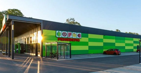 Feneberg Supermarkt Außenansicht Ein moderner Feneberg Supermarkt mit grüner und gelber Außenfassade, einem Fahrradunterstand und einem Parkplatz bei Sonnenaufgang oder Sonnenuntergang.