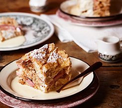 Scheiterhaufen mit Vanillesauce Ein Teller mit einem Stück Scheiterhaufen, serviert mit Vanillesauce, auf einem rustikalen Holztisch.