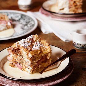 Scheiterhaufen mit Vanillesauce Ein Teller mit einem Stück Scheiterhaufen, serviert mit Vanillesauce, auf einem rustikalen Holztisch.