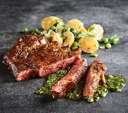Gegrilltes Steak mit Kräutersauce und Kartoffelsalat Ein saftiges Steak, in Scheiben geschnitten, mit einer grünen Kräutersauce und Kartoffelsalat mit Erbsen.