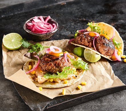 Bean & Beef Tacos Bean & Beef Tacos mit gegrilltem Rindfleisch, Bohnen, Mais und frischen Salatblättern, garniert mit eingelegten roten Zwiebeln und Limettenscheiben.