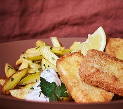 Paniertes Fischfilet mit Pommes Frites und Zitronenscheiben Paniertes Fischfilet mit Pommes Frites, Zitronenscheiben und einer Kräutersoße, garniert mit frischer Petersilie.