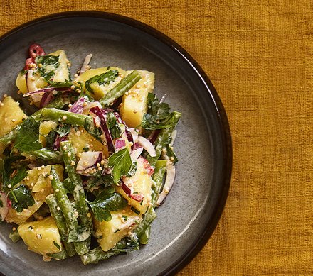 Kartoffelsalat mit grünen Bohnen und Kräutern Ein Teller mit Kartoffelsalat, grünen Bohnen, roten Zwiebeln und frischen Kräutern, garniert mit Senfkörnern.