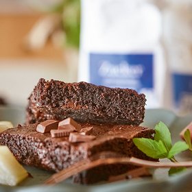 Saftige Schokoladen-Brownies Ein Teller mit zwei Stücken saftiger Schokoladen-Brownies, garniert mit Schokoladenstückchen und Minzblättern.
