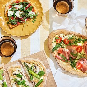 Brätscher Verschiedene belegte Flammkuchen auf einem gedeckten Tisch, serviert mit Getränken in Gläsern.