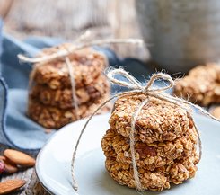 Haferkekse mit Mandeln Gestapelte Haferkekse, mit einem Bindfaden zusammengebunden, auf einem Teller, im Hintergrund weitere Keksstapel und Mandeln.