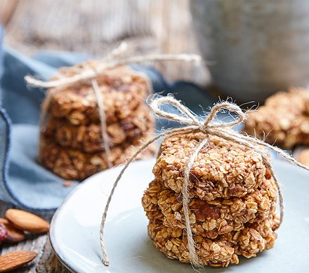 Haferkekse mit Mandeln Gestapelte Haferkekse, mit einem Bindfaden zusammengebunden, auf einem Teller, im Hintergrund weitere Keksstapel und Mandeln.