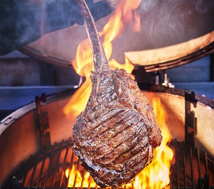 Gegrilltes Tomahawk-Steak über offenen Flammen Ein großes Tomahawk-Steak wird über einem offenen Grill mit hohen Flammen gegrillt.