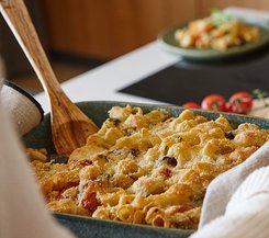 Bunter Gemüseauflauf Ein frisch gebackener Gemüseauflauf mit einer goldbraunen Kruste, serviert in einer grünen Auflaufform, mit einem hölzernen Servierlöffel.