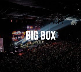 Big Box Menschenmenge bei einem Konzert in der Big Box. Eine große Menschenmenge genießt eine Live-Performance auf einer Bühne, die von bunten Lichtern und großen Bildschirmen beleuchtet wird.