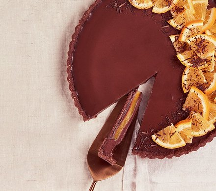 Schokoladentarte mit Orange Eine Schokoladentarte mit Orangenscheiben, ein Stück wurde herausgeschnitten und liegt auf einem Servierheber.