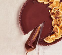 Schokoladentarte mit Orange Eine Schokoladentarte mit Orangenscheiben, ein Stück wurde herausgeschnitten und liegt auf einem Servierheber.