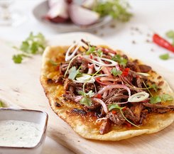 Fladenbrot mit zerkleinertem Rindfleisch und Koriander Fladenbrot mit zerkleinertem Rindfleisch, roten Zwiebeln, Frühlingszwiebeln und frischem Koriander, serviert auf einem Holzbrett.