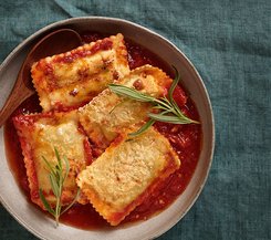 Ofenmaultaschen in Tomatensauce Ein Teller mit Ofenmaultaschen in Tomatensauce, garniert mit frischen Kräutern.