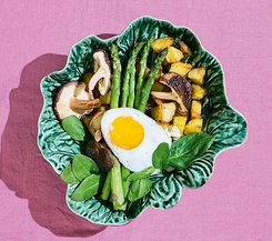 Gebratenes Gemüse mit Spargel und Spiegelei Ein Teller mit gebratenem Gemüse, Pilzen, Spargel und einem Spiegelei, angerichtet auf einem grünen, blattförmigen Teller.