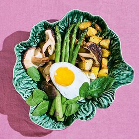 Gebratenes Gemüse mit Spargel und Spiegelei Ein Teller mit gebratenem Gemüse, Pilzen, Spargel und einem Spiegelei, angerichtet auf einem grünen, blattförmigen Teller.