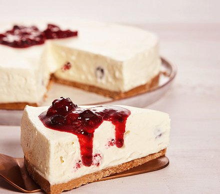 Käsekuchen mit roter Beeren-Sauce Ein Stück Käsekuchen mit roter Beeren-Sauce, das von einem ganzen Käsekuchen auf einem Teller geschnitten wurde.