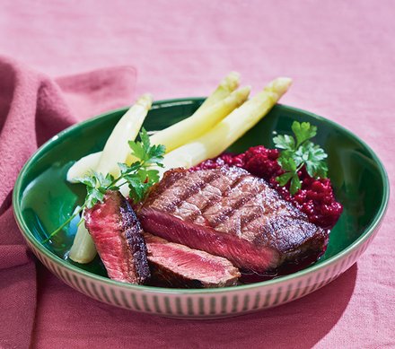 Gegrilltes Steak mit weißem Spargel und roter Beilage Ein Teller mit gegrilltem Steak, weißen Spargelstangen und einer roten Beilage, garniert mit frischen Kräutern.