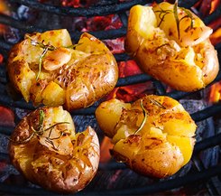 Gegrillte zerdrückte Kartoffeln mit Rosmarin und Knoblauch Knusprige, zerdrückte Kartoffeln auf einem Grillrost über glühenden Kohlen, garniert mit Rosmarin und Knoblauch.
